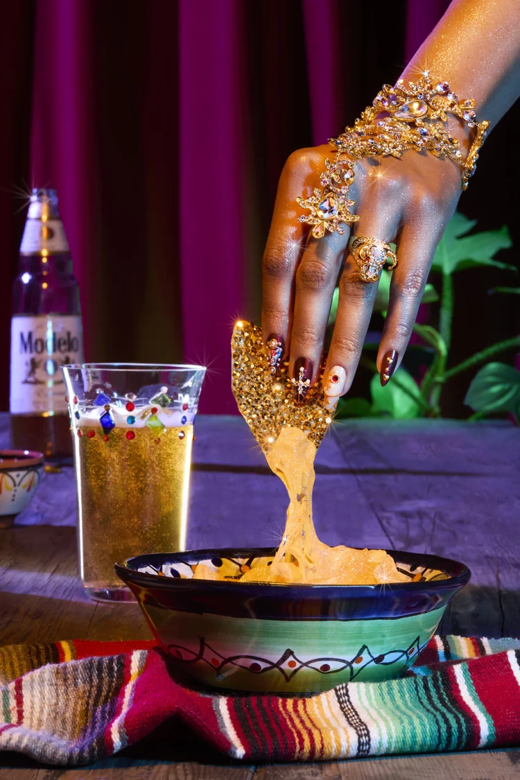 Hand reaching into cheesy nachos, Modelo on the table